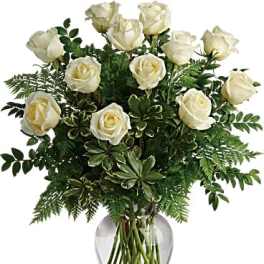 White roses in a clear glass vase with mixed greenery