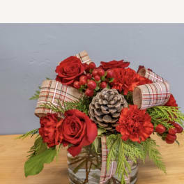Red roses and carnations arranged in a glass vase with plaid ribbon and a pinecone