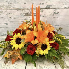 Orange lilies and red roses with sunflowers in a low arrangement.