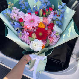 Colorful mixed bouquet with gerbera daisies, tulips, and blue flowers wrapped in mint paper