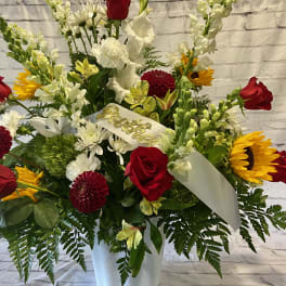 Red roses, sunflowers, and white flowers in a white vase with a ribbon