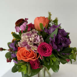 Mixed bouquet of roses, carnations, and purple blooms in a glass vase
