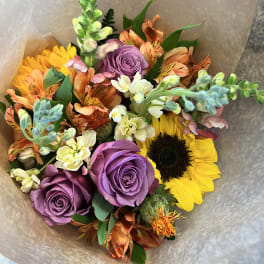 Bouquet of purple roses, sunflowers, and orange mixed blooms wrapped in paper