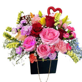 Mixed bouquet of roses, carnations, and lilies in a black gift bag with a red heart topper