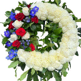 Heart-shaped floral wreath with white chrysanthemums, red and white roses, and blue flowers