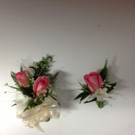 Two pink rose boutonnieres with white flowers and ribbon accents
