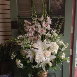 Tall white floral arrangement in a wicker basket with lilies and orchids