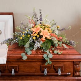 Large floral spray on a wooden casket with peach lilies and mixed blooms