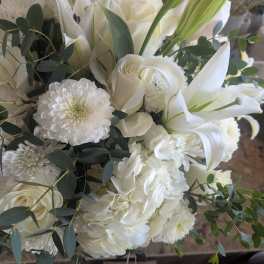 All-white arrangement of roses, lilies, hydrangeas, and mums with cascading greenery