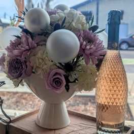 Lavender and white flower arrangement with white ornaments beside a rose sparkling wine bottle