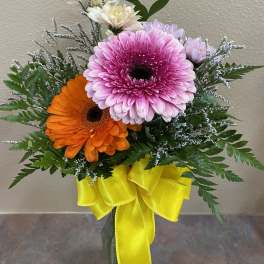 Pink and orange gerbera daisies in a glass vase with a yellow ribbon