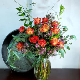 Orange and red roses in a clear glass vase with airy greenery