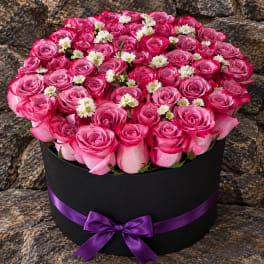 Pink rose arrangement in a black round box with a purple ribbon