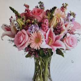 Pink roses, lilies, and gerbera daisies arranged in a clear glass vase