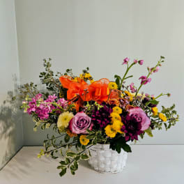 Mixed bouquet in a white woven basket with an orange ribbon
