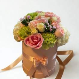Pink and cream roses arranged in a round hatbox with satin ribbon