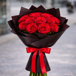 Bouquet of red roses wrapped in dark paper with a red satin bow