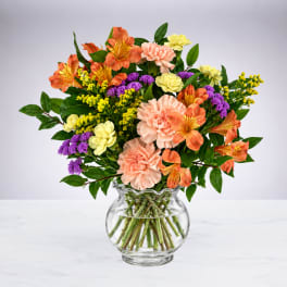 Mixed bouquet of orange, pink, yellow, and purple flowers in a glass vase