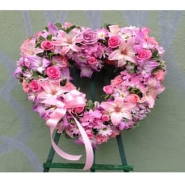 Heart-shaped pink floral wreath on a stand with ribbon