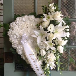 White funeral wreath with lilies and roses and a ribbon reading Loving Mother