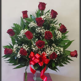 Red roses arranged in a clear vase with baby's breath and a red ribbon