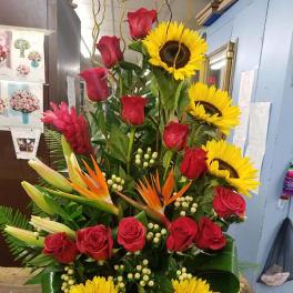 Tall arrangement of red roses, sunflowers, and tropical blooms