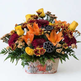 Autumn floral arrangement with orange lilies and yellow roses in a pumpkin-decorated container
