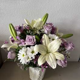 Bouquet of white lilies, lavender roses, and white daisies in a white vase
