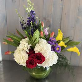 Mixed bouquet in a green glass vase with white hydrangeas, red roses, and yellow calla lilies