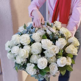 Large bouquet of white roses with greenery being held by a person