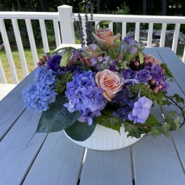 Low floral arrangement with pink roses and purple hydrangeas in a white bowl