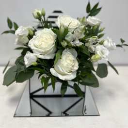White roses and small white blooms arranged in a square glass vase