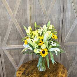 Bouquet of white lilies, yellow roses, and sunflowers in a clear glass vase