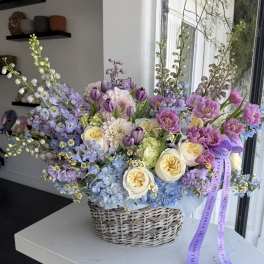 Pastel floral arrangement in a woven basket with purple ribbon