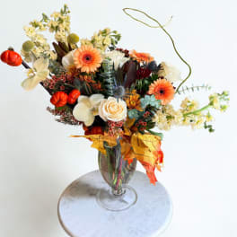 Autumn bouquet with orange gerberas, white roses, and cream orchids in a glass vase