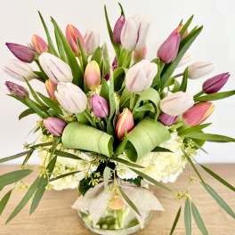 Pink and white tulips arranged in a glass vase with a burlap bow