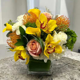 Yellow orchids and roses arranged in a square glass vase