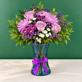 Pink and purple mixed bouquet in a blue glass vase with a purple ribbon