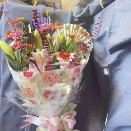 Bouquet of mixed flowers wrapped in floral paper with a pink ribbon
