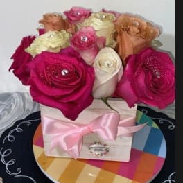 Pink and cream roses arranged in a box with a pink ribbon