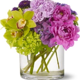 Bouquet of purple and pink flowers with green orchids in a clear glass vase