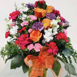 Mixed bouquet of roses, carnations, and white filler flowers in a gold vase with orange ribbon