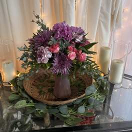Purple and pink floral arrangement in a mauve vase with candles nearby