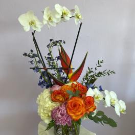Mixed floral arrangement with white orchids and orange roses in a glass vase
