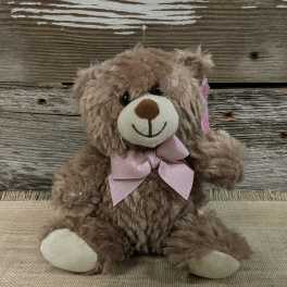 Brown teddy bear with a pink bow sitting on burlap