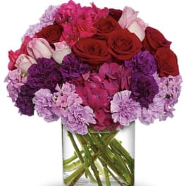 Bouquet of red roses and pink-purple flowers in a clear glass vase