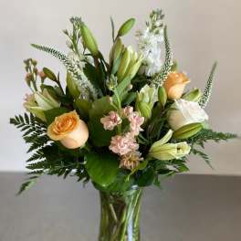 Tall bouquet of peach roses, white lilies, and soft pink flowers in a clear glass vase