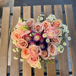 Heart-shaped bouquet of pink and peach roses with small white daisies