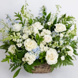 Large white and pale blue flower arrangement with roses in a wicker basket