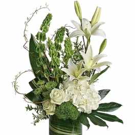 Tall white and green arrangement with lilies, hydrangeas, and roses in a clear cylinder vase